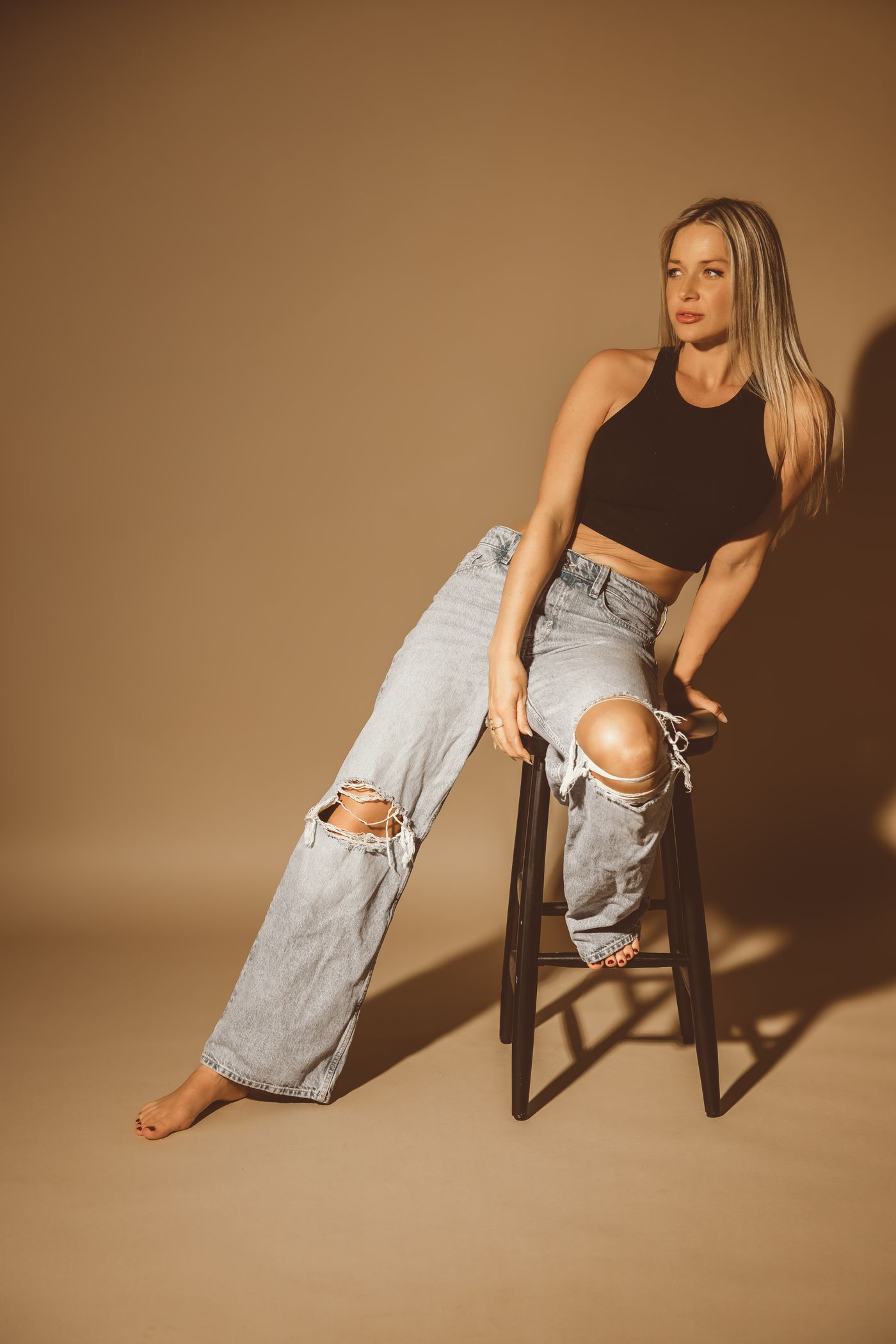 Jillian Phyllis barefoot on a black stool, glancing away from the camera.