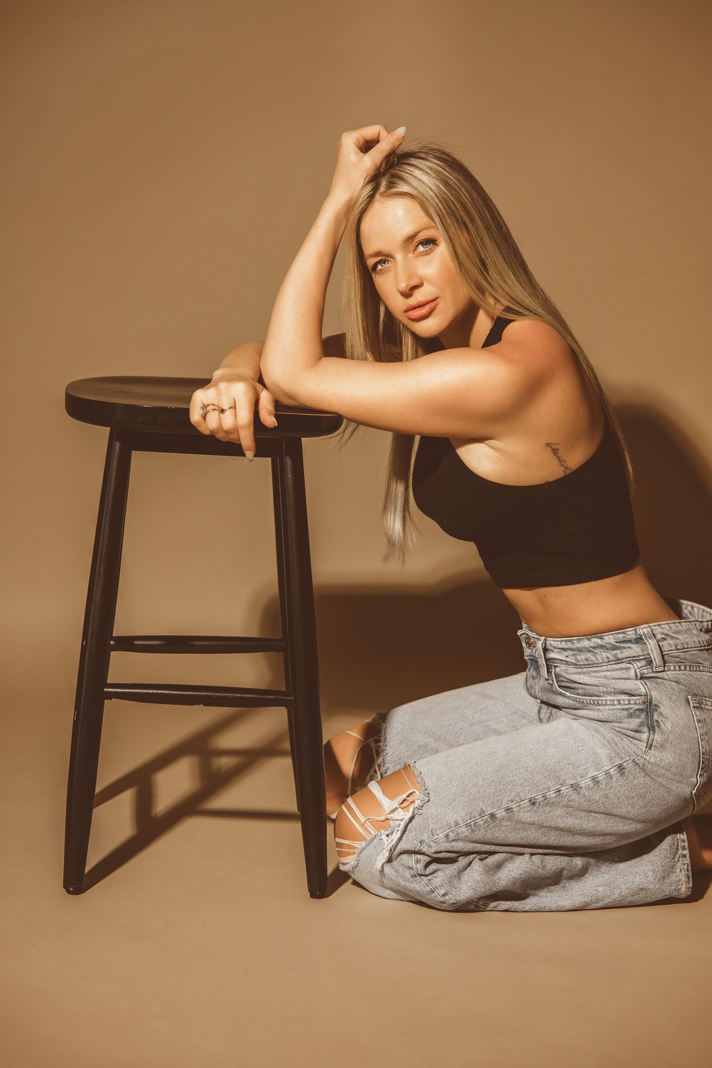Jillian Phyllis kneeling beside a black stool, looking straight into the camera.