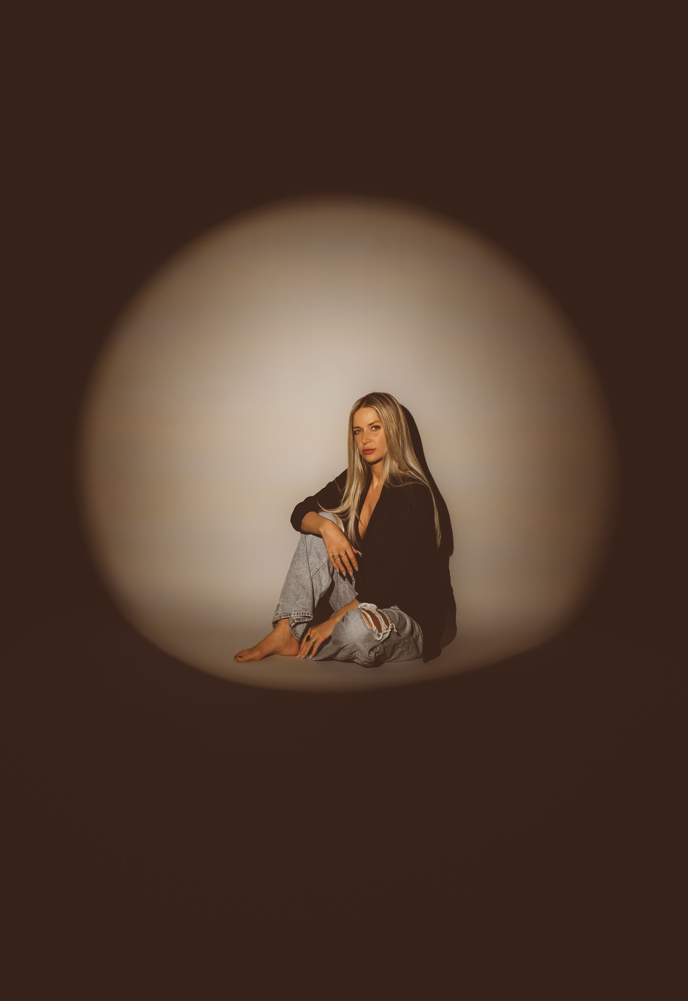 Jillian Phyllis seated alone in a circle of spotlight on a dark stage.